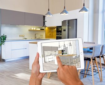 Hands holding tablet with kitchen interior sketch. In the background real finished kitchen interior design. Kitchen presentation.